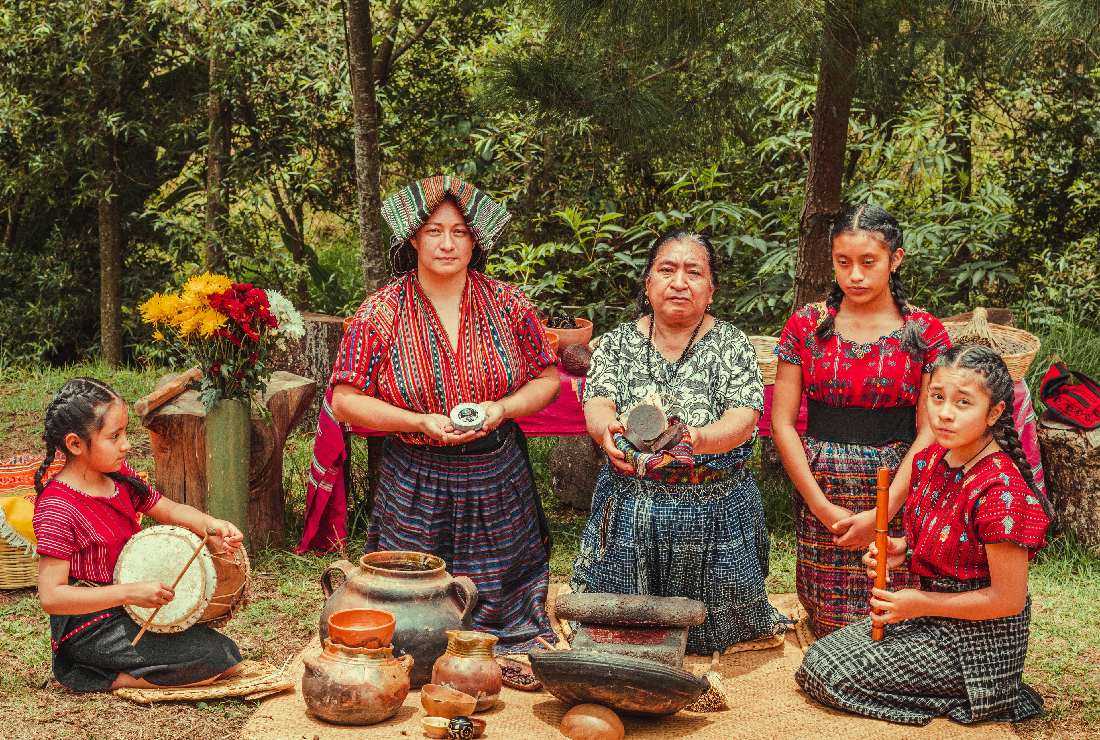 Maya Frauen verschiedener Generationen präsentieren den zeremoniellen Kakao mit Musik. Man sieht das traditionelle Mahlwerkzeug, eine kleine Steinmühle (Metate).