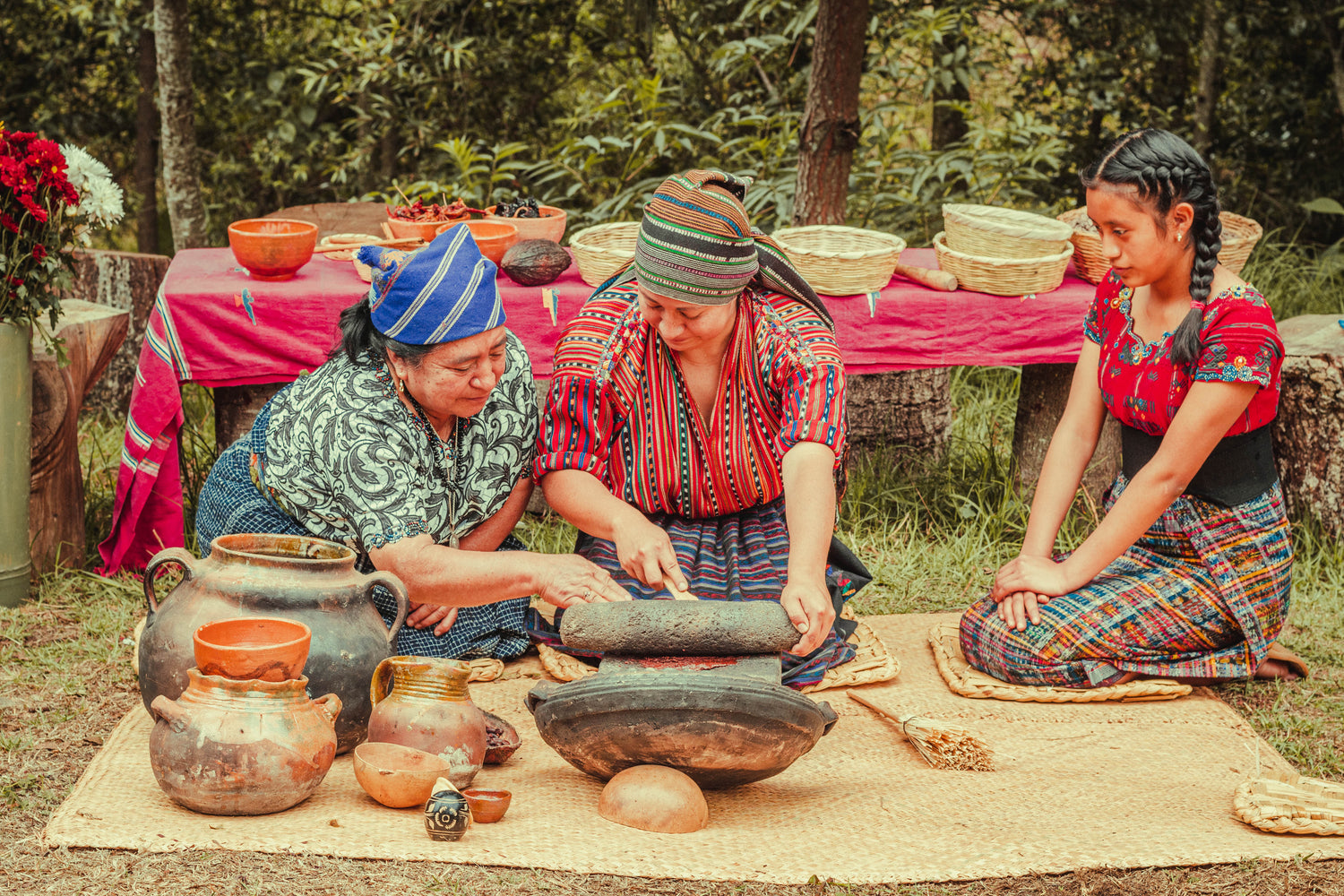 Maya Frauen aus Guatemala verschiedener Generationen bei der traditionellen Verarbeitung der Kakaopaste mit einer Steinmühle