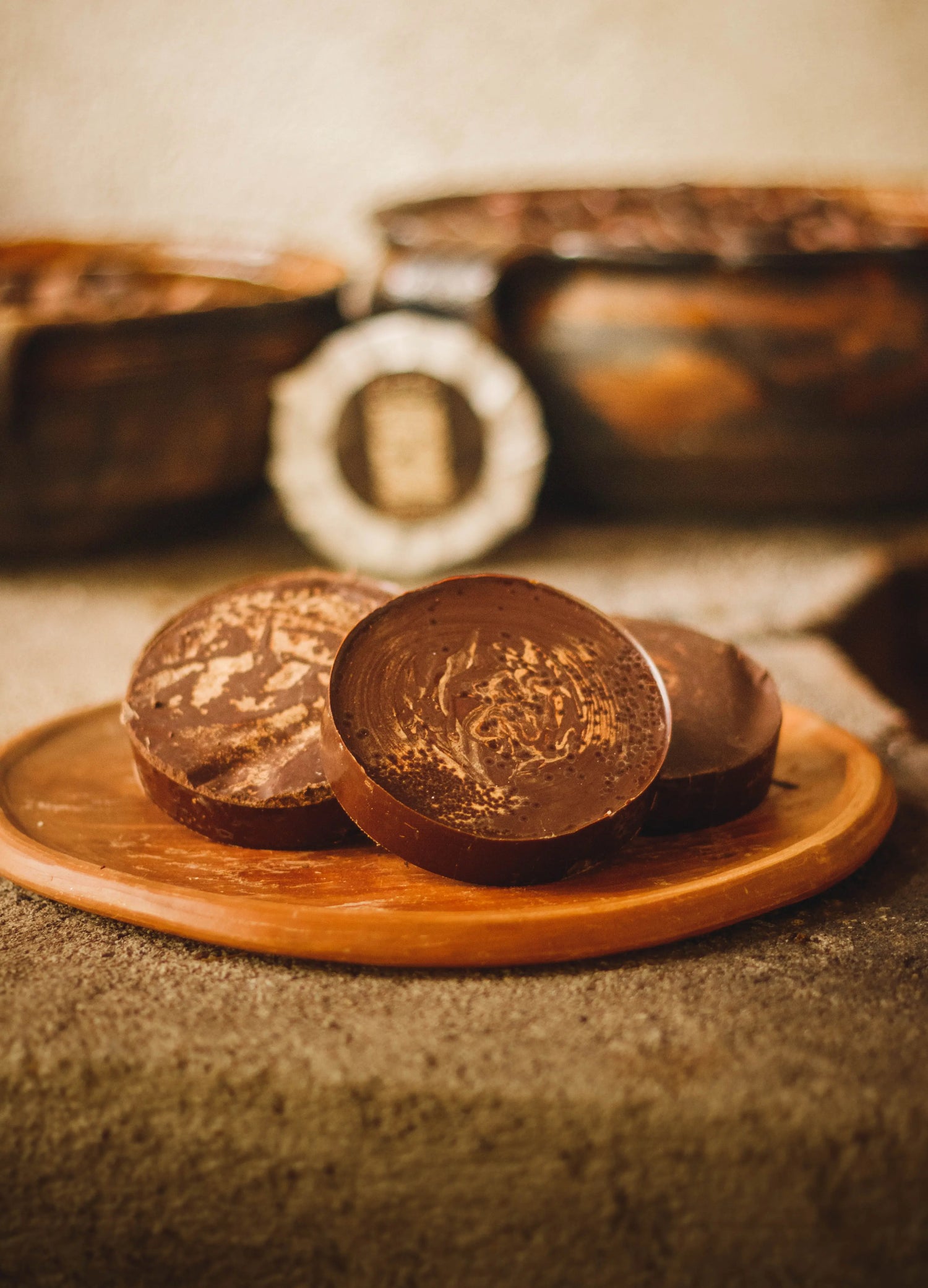 Three blocks of ceremonial cacao on a plate with bowls of roasted cacao beans in the background