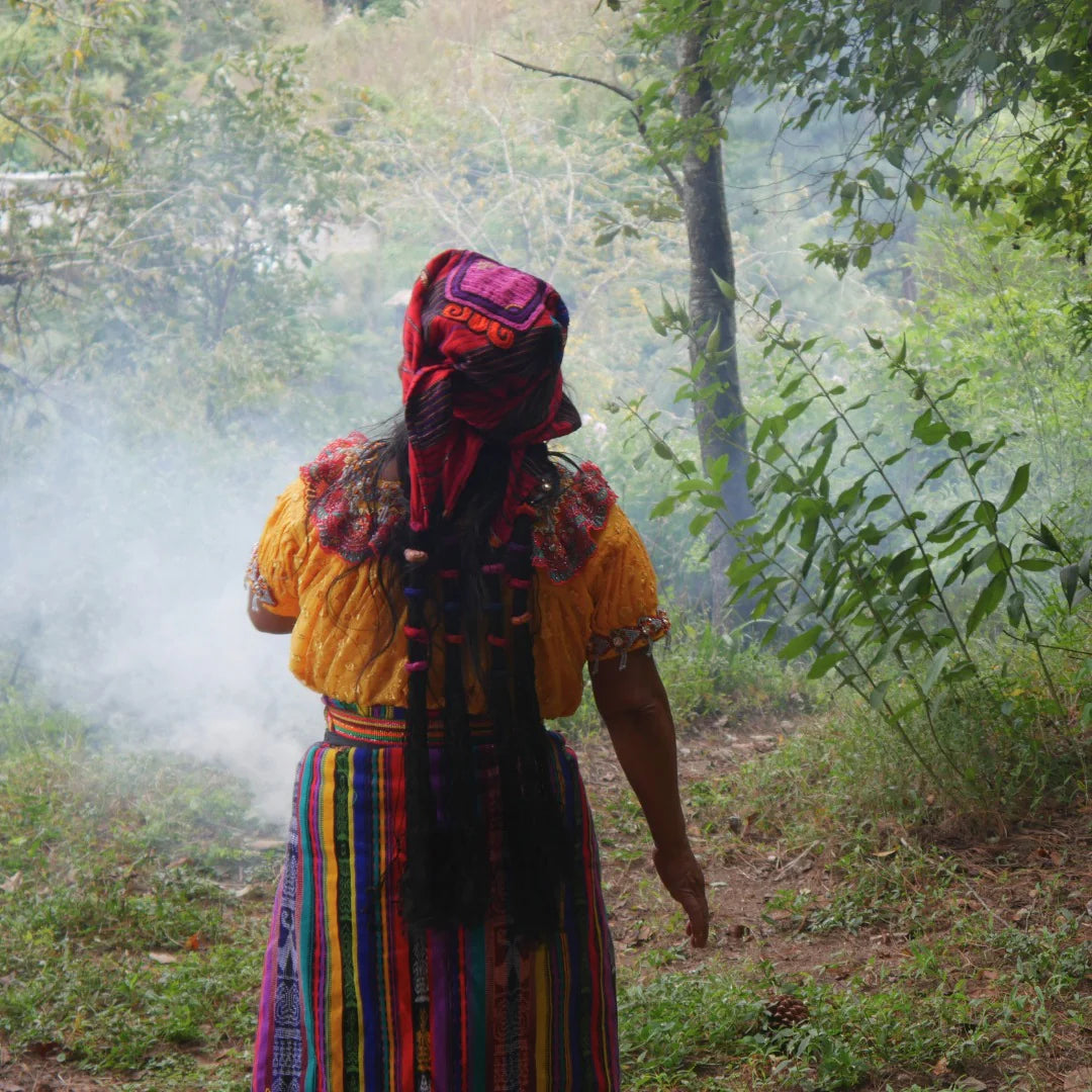 Maya woman in traditional clothes walking towards the jungle, surrounded by smoke from incense